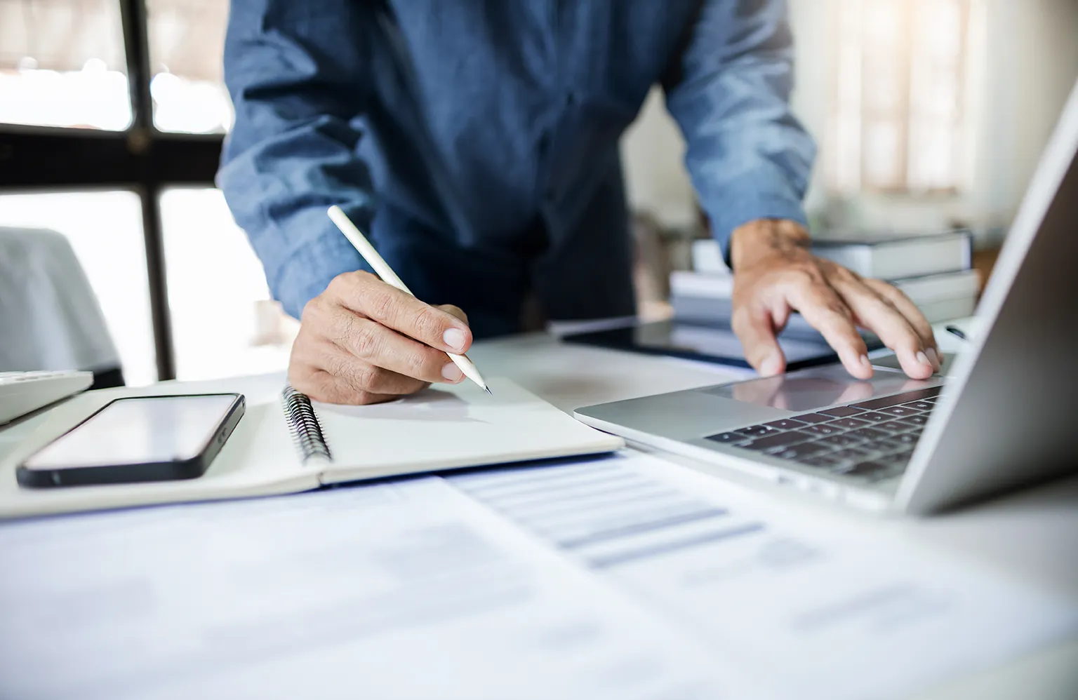 Profissional registra cálculos de impostos no caderno e no laptop — conceito de split payment na Reforma Tributária 2025.