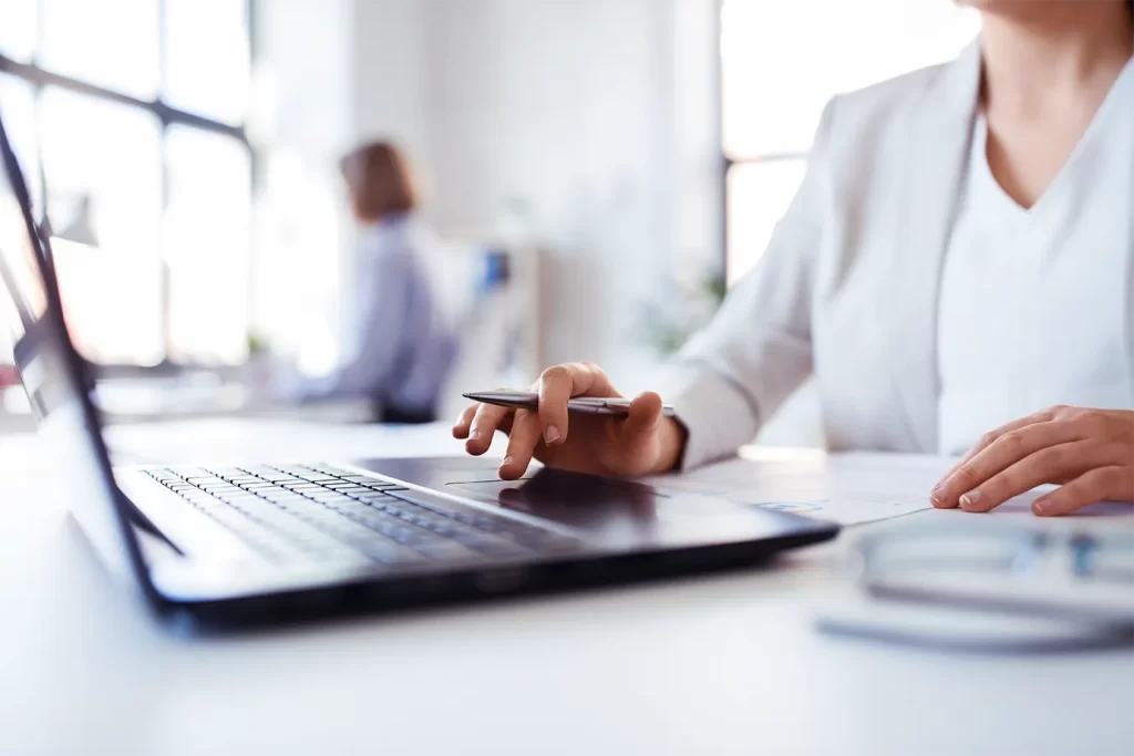 Profissional analisando no notebook documentos e números do fechamento das demonstrações financeiras